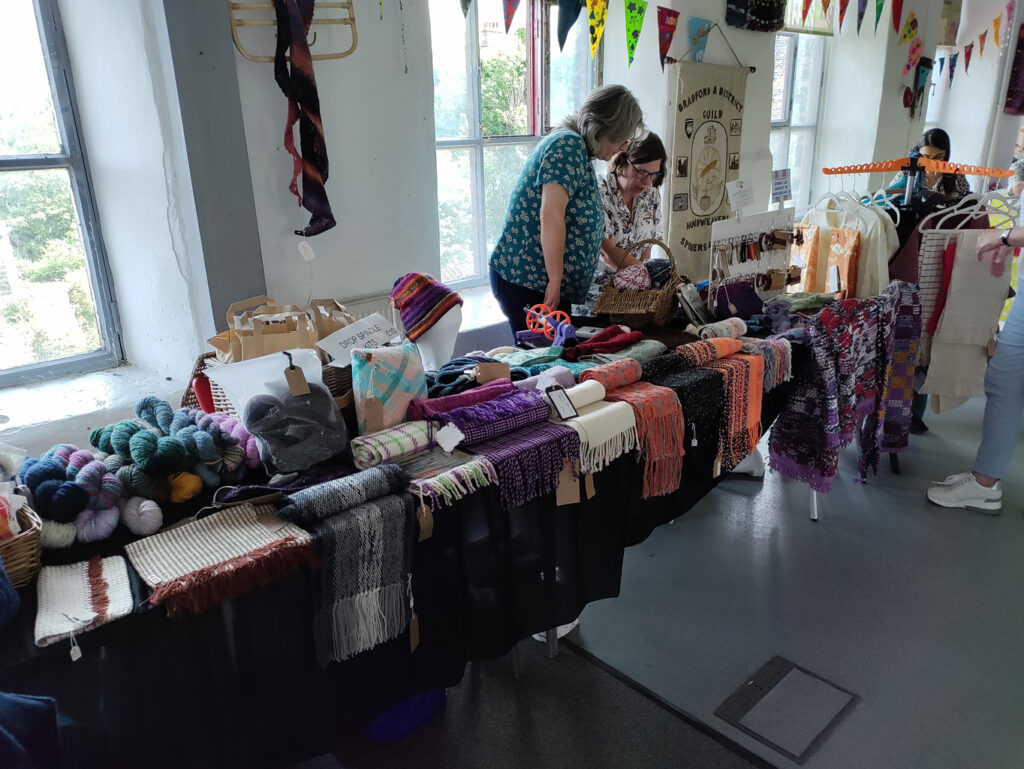A table full of spun yarn, woven scarves, and knitted items.