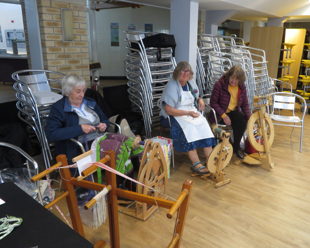 Three women, three spinning wheels, and a floor inkle loom
