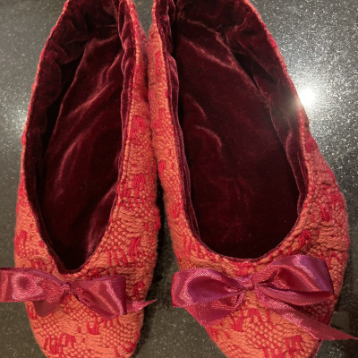 A pair of red and pink woven slippers with red linings and bows.