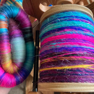 Spinning wheel bobbin full of colourful handspun yarn, in blues, pinks, purples and yellow